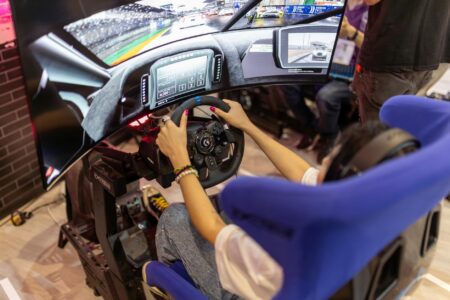 How Racing Wheel Force Feedback Technology Reached Console-Quality Standards Professional racing wheel and pedal setup on gaming desk with multiple monitors