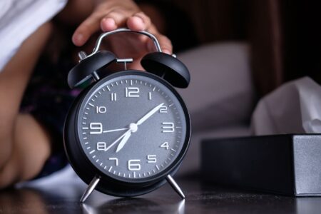 Nintendo’s Alarm App Is Quietly Becoming a Sleep Tracking Platform A modern alarm clock sitting on a bedroom nightstand beside a lamp