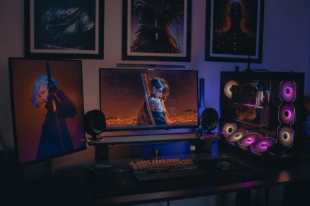 Palworld’s Survival Formula Is Luring Ark Players Back A gaming PC setup with multiple monitors displaying a colorful open-world survival game environment