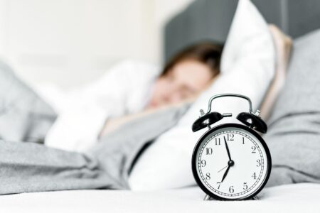A modern alarm clock sitting on a bedside table in a softly lit bedroom