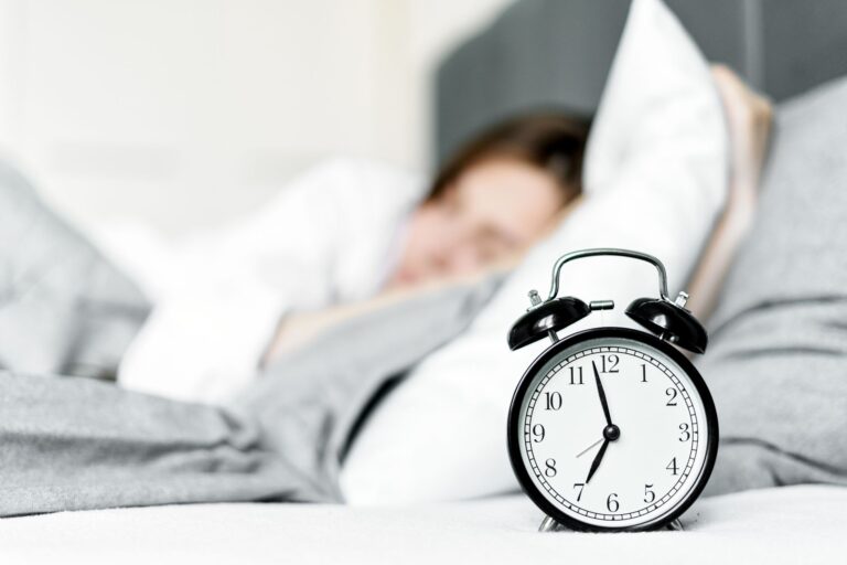 A modern alarm clock sitting on a bedside table in a softly lit bedroom
