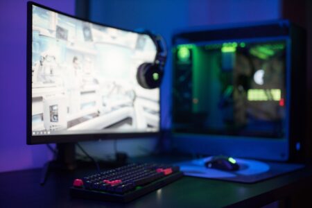 A gaming PC setup with a glowing monitor displaying a multiplayer game in a dark room