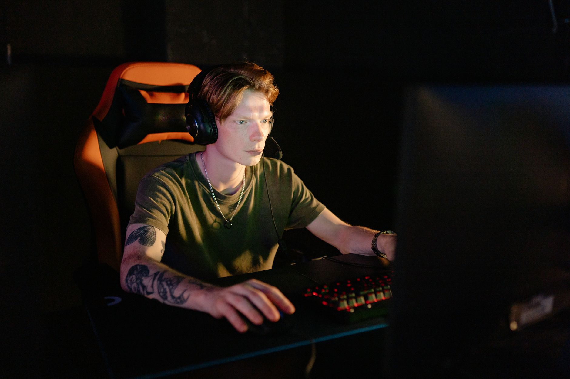 A person playing a PC game at a desk with a monitor glowing in a dark room