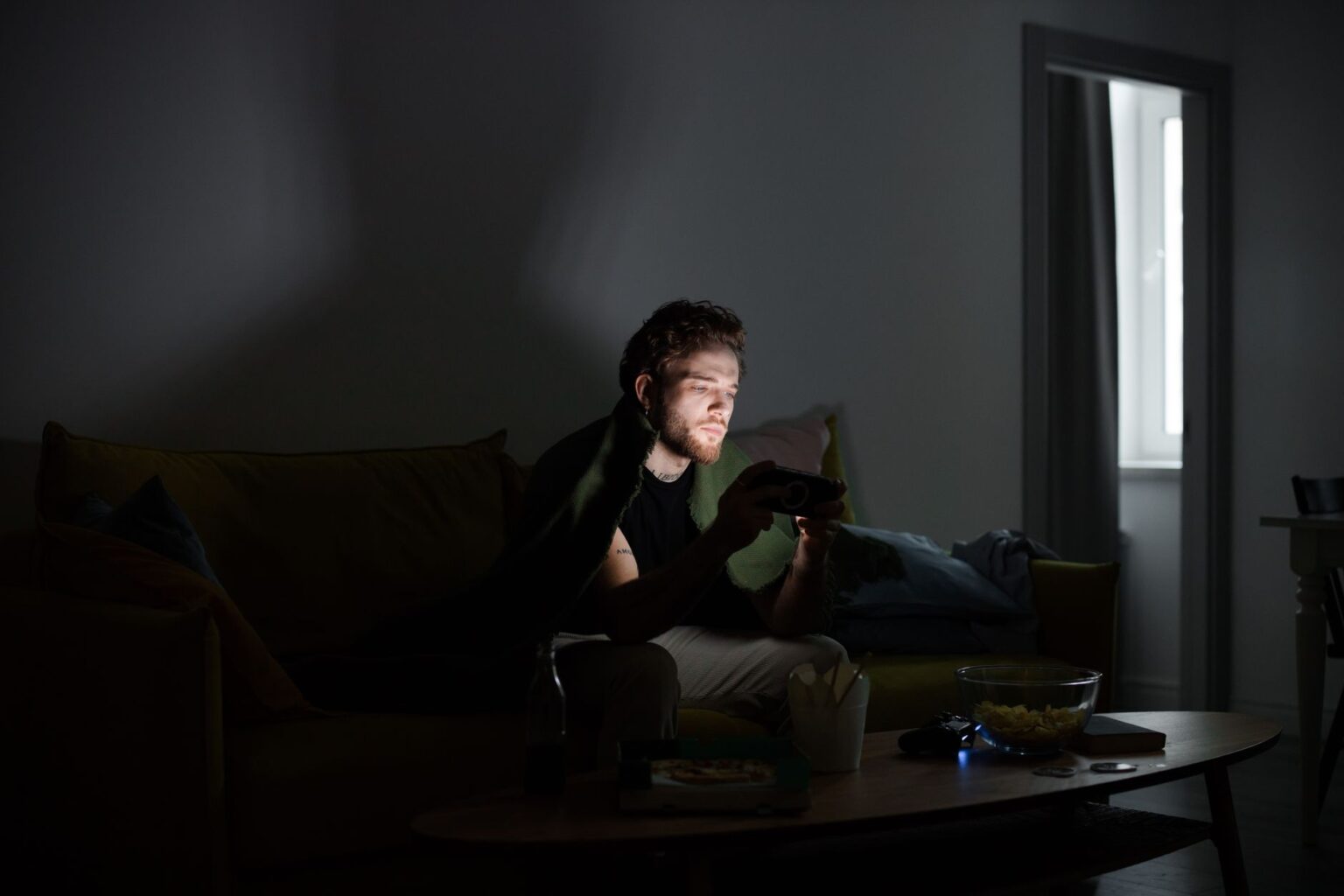 A gamer sitting in a dark room illuminated by monitor light, focused on screen