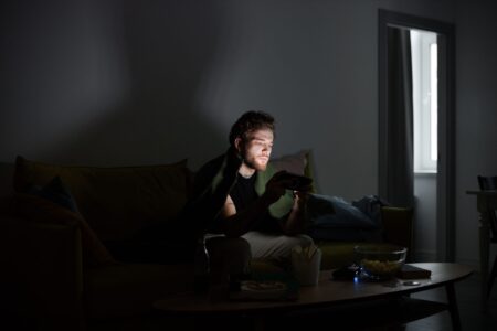 A gamer sitting in a dark room illuminated by monitor light, focused on screen