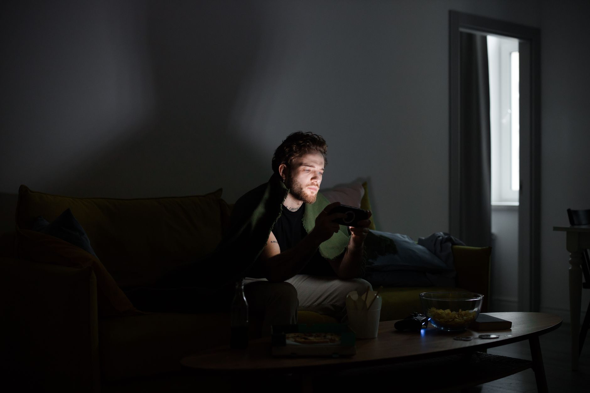 A gamer sitting in a dark room illuminated by monitor light, focused on screen